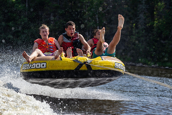 Three teens having tubing madness fun behind a boat