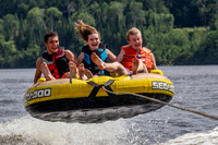 Three kids catching air in a tube being pulled behind a boat