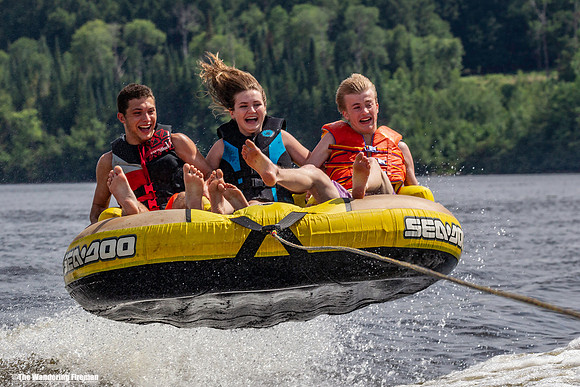 Three kids catching air in a tube being pulled behind a boat