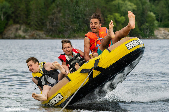 Three boys on a tube being pulled behind a boat about to flip over