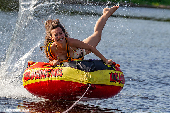 Pretty girl hangs on to her tube behind a boat