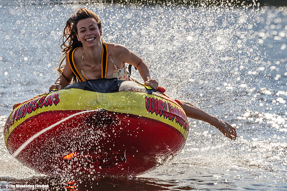 Smiling girl rides a tube behind a boat and water spray