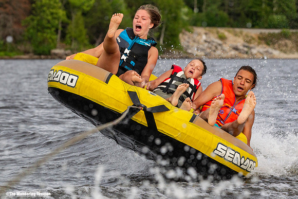 Three youths looking scared being pulled behind a tube behind a boat