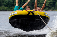 Three boys catch massive air while riding a tube behind a boat
