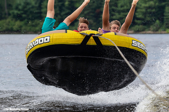 Three boys catch massive air while riding a tube behind a boat